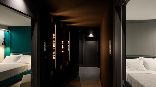 Un couloir d’hôtel avec un lit sur la gauche, un mini-bar et une porte au fond.
