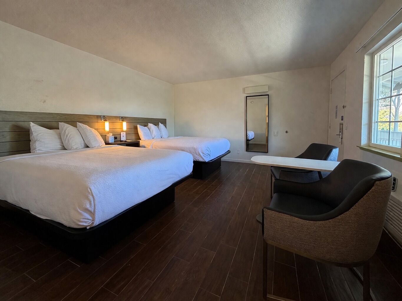 Une chambre d’hôtel avec deux lits, un bureau, une chaise, un miroir et une fenêtre.