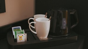 Una estación de café con dos tazas blancas, una cafetera negra y algunos sobres de café sobre una bandeja.