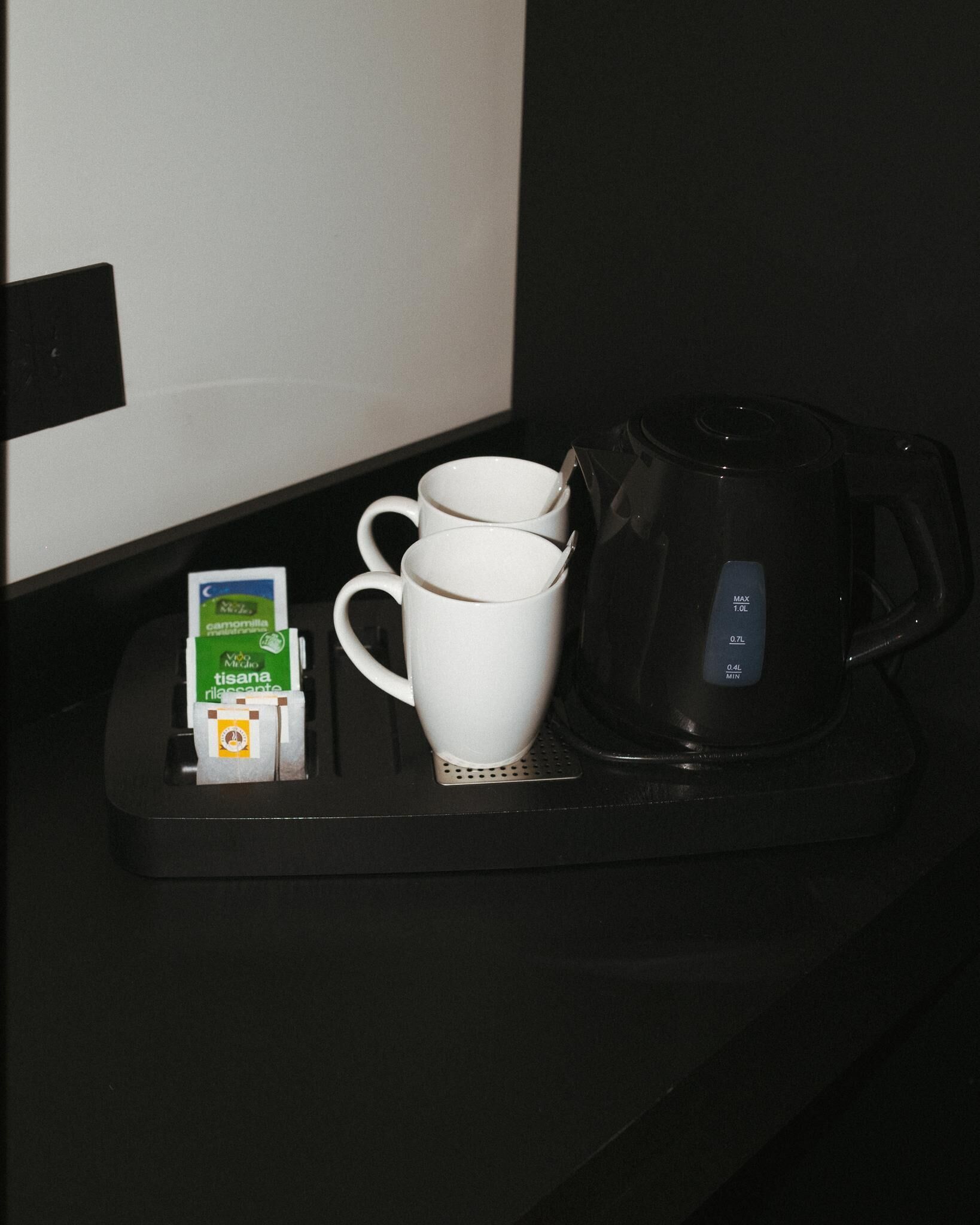 Une machine à café, deux tasses blanches et une boîte de café Tisana, le tout posé sur un plateau noir.