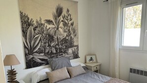 A bedroom with a bed, a nightstand, a lamp, a framed picture, and a large botanical tapestry on the wall. - Pleasant vacation home for 4 people near the beach Biscarrosse lake (Biscarrosse)