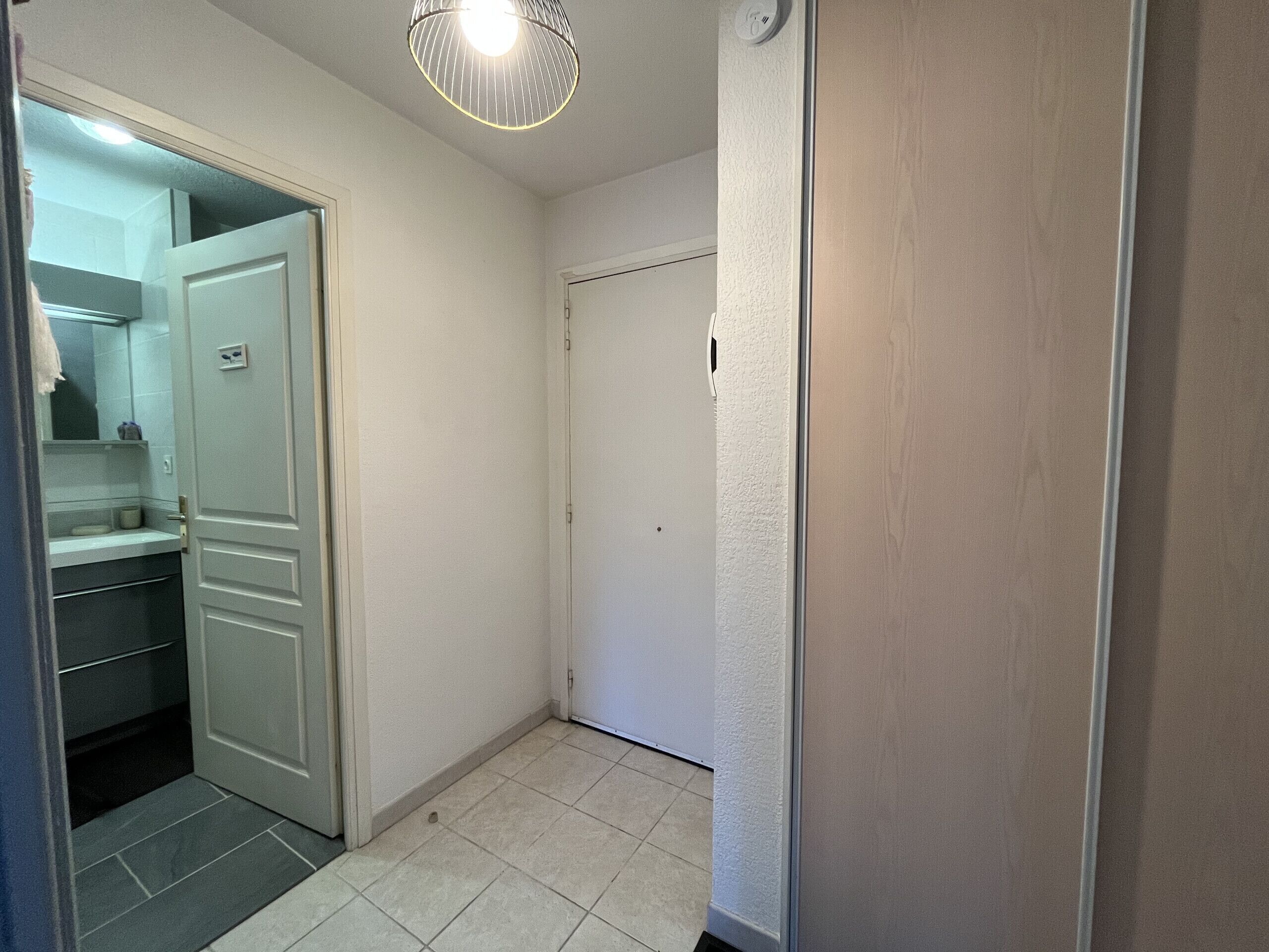 A hallway with a white door, a small bathroom with a mirror, and a light fixture.