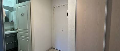A hallway with a white door, a small bathroom with a mirror, and a light fixture.