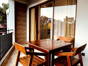 A wooden table with four chairs on a balcony with a view of greenery. - Eyeful Ella (Ella)