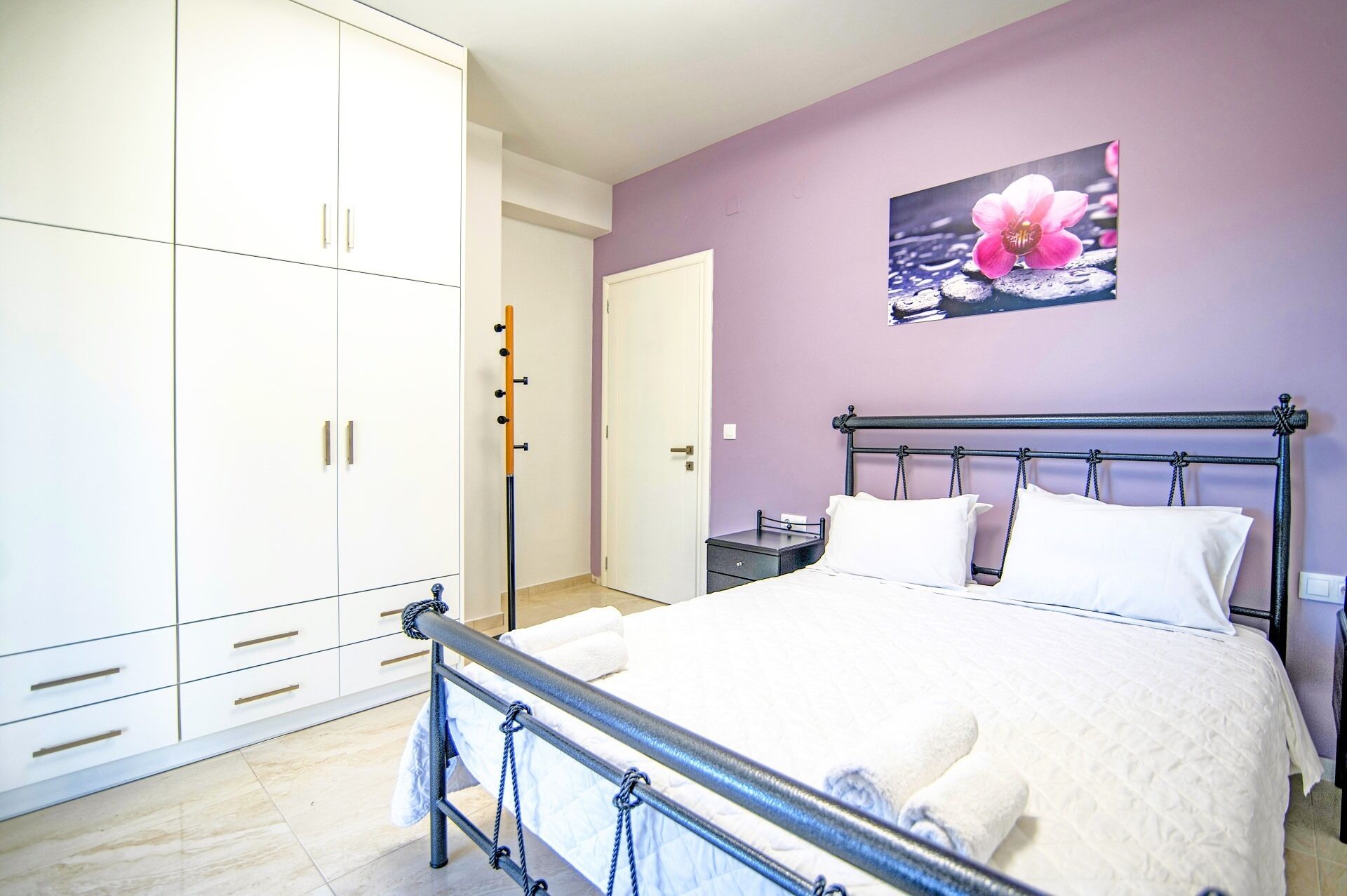 A bedroom with a bed, white wardrobe, and a painting of a flower on the wall.