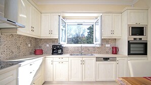 Eine Küche mit hellen Holzschränken, einem Fenster mit Ausblick, einem roten Toaster, einer Kaffeemaschine und einem Bosch Geschirrspüler.