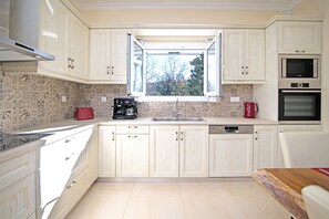 A kitchen with light wooden cabinets, a window with a view, a red toaster, a coffee maker, and a Bosch dishwasher. - Villa Alegria a Casa II by Villa Plus (Ionian Islands)