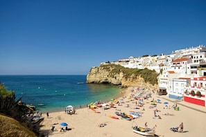 A beach with white buildings, clear blue water, and people sunbathing. - Villa Figueiras by Villa Plus (Lagoa)