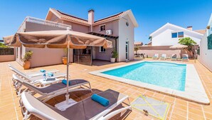 En bostadsfastighet med en swimmingpool, solstolar och en täckt uteplats.