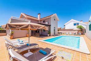 Ein Wohnhaus mit Schwimmbad, Liegestühlen und einer überdachten Terrasse.