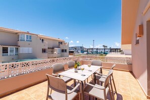 Eine Terrasse mit Tisch und Stühlen, im Hintergrund ein Pool und Blick auf andere Gebäude.