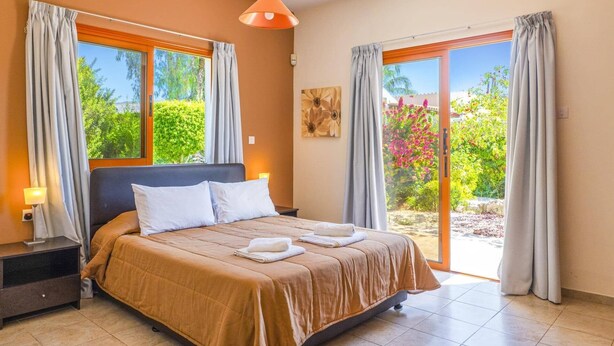 A bedroom with a bed, a nightstand, a lamp, and a painting on the wall. - Villa Nicola by Villa Plus (Peyia)