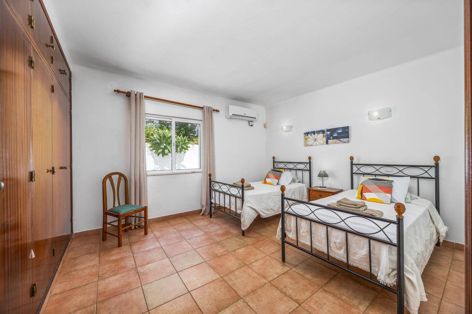 Ein Schlafzimmer mit zwei Betten, einem Holzschrank, einem Stuhl und einem Fenster mit Vorhängen.