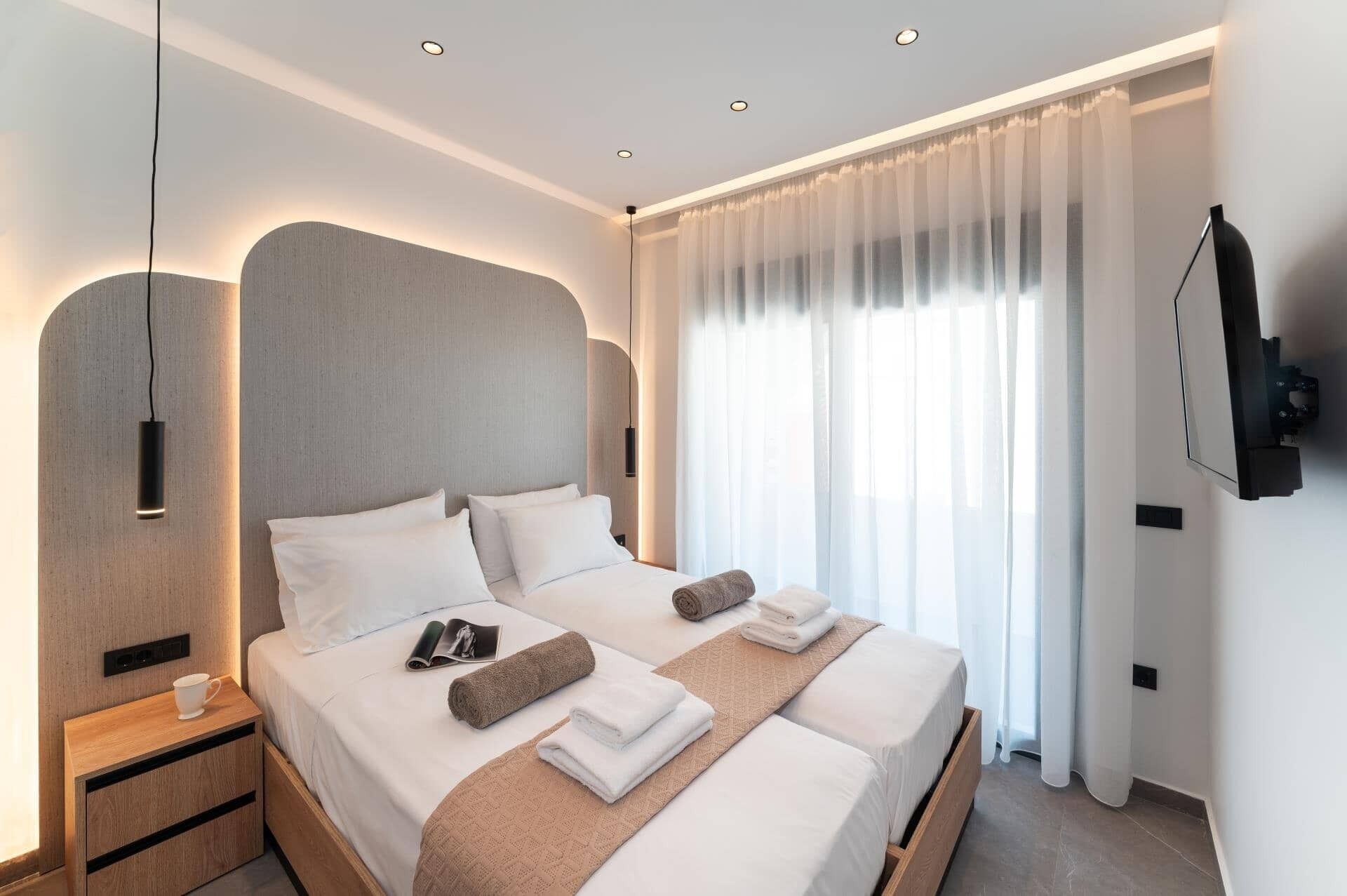 Een moderne hotelkamer met een groot bed, nachtkastjes, een flatscreen televisie en een groot raam met dunne gordijnen.