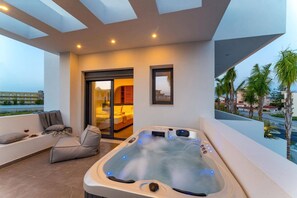 Ein moderner Balkon mit Whirlpool, einer Sitzecke mit Kissen und Blick auf Palmen und Gebäude.