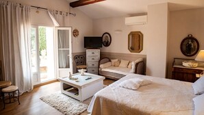 Un dormitorio con cama, televisor, cómoda, silla y ventana con cortinas.