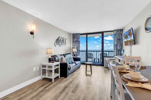 A modern living room with a sofa, dining table, and a balcony with a view. - Compass Cove Condos (Myrtle Beach)