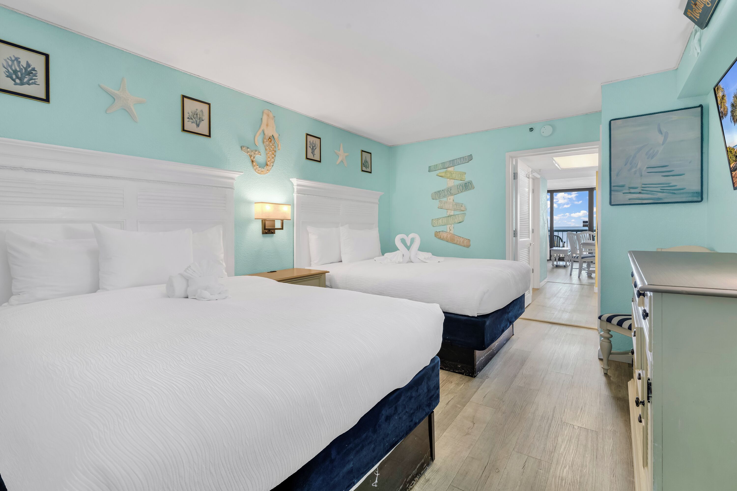 Une chambre avec deux lits, une coiffeuse et vue sur la plage.
