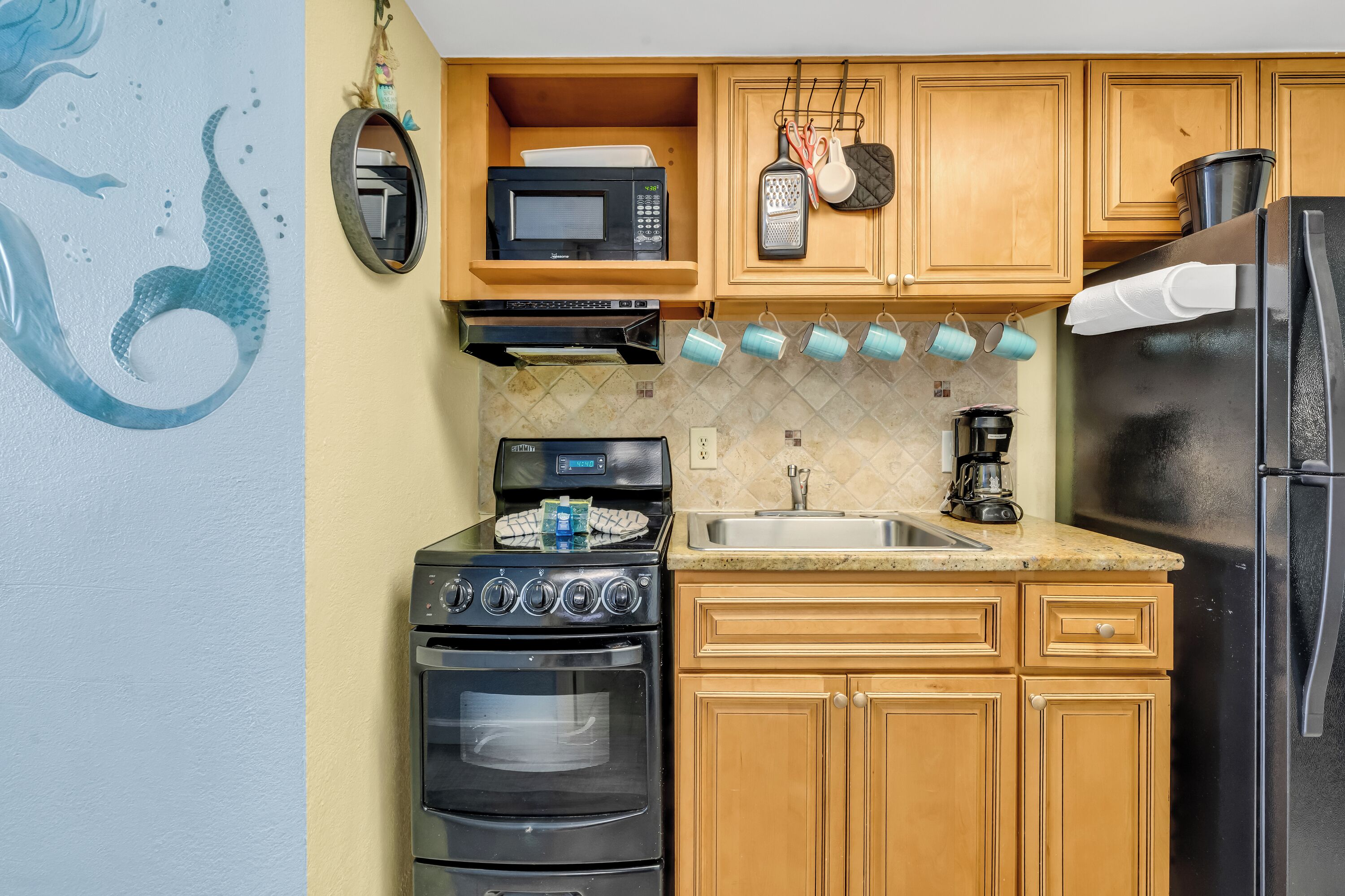 A kitchen with wooden cabinets, a black stove, a microwave, and a refrigerator.