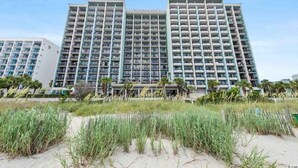 A high-rise hotel with multiple balconies, located near a beach with grassy areas. - Compass Cove Condos (Myrtle Beach)