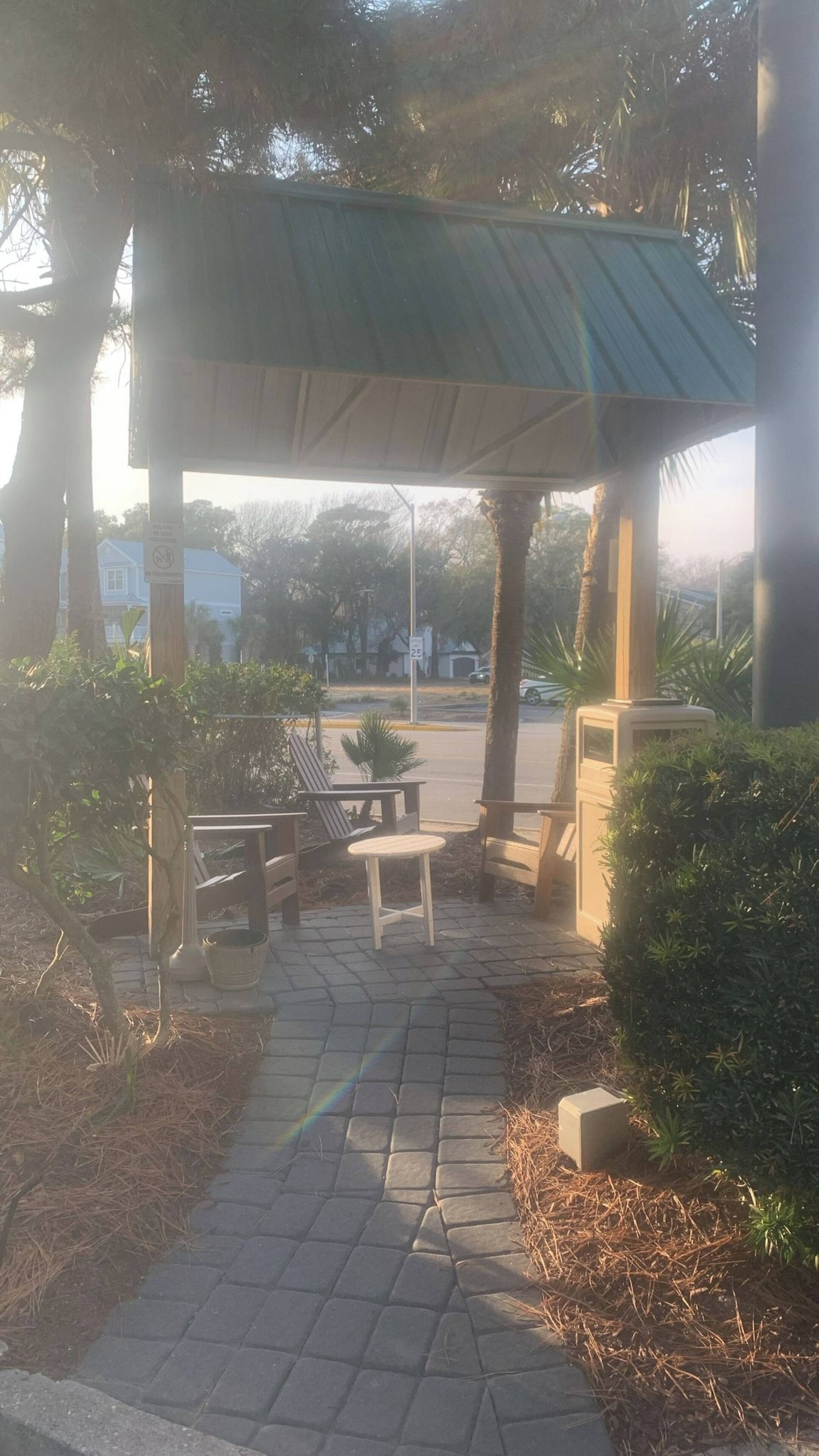Un espace extérieur abrité, doté de bancs et de tables, et entouré d’arbres et d’arbustes.