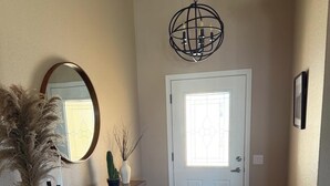 A hallway with a white door, a mirror, a wooden console table with decorative items, and a patterned rug.