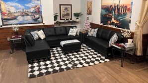 Un salon avec un canapé d’angle en cuir noir, un tapis à carreaux noirs et blancs et un grand tableau représentant un paysage urbain.