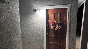Une porte en bois, un paillasson, une plaque de numéro de maison et un arrangement floral.