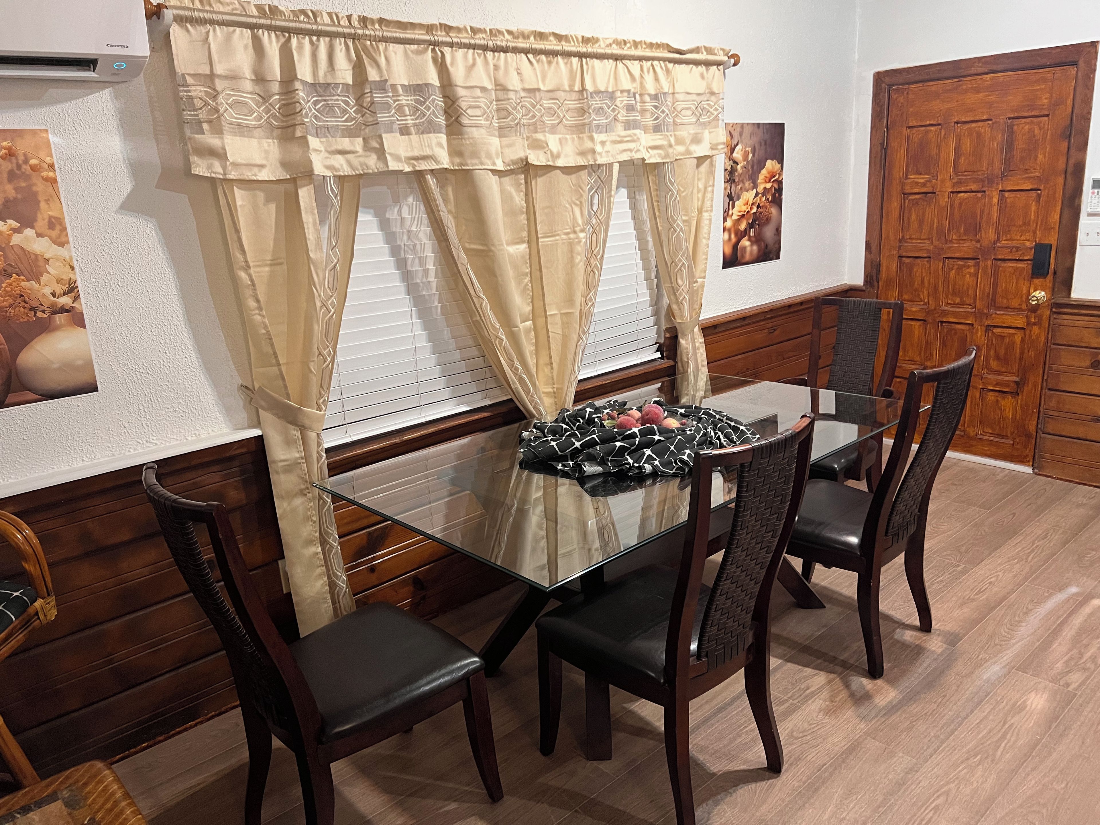 A dining area with a glass table, dark wooden chairs, and a patterned curtain.