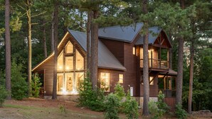 A log cabin with a large front porch, multiple windows, and a balcony. - Pickleball Cabin + Fun Group Getaway (Broken Bow)