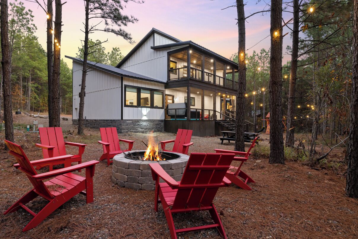Eine Holzhütte mit Feuerstelle und roten Adirondack-Stühlen inmitten von Bäumen.