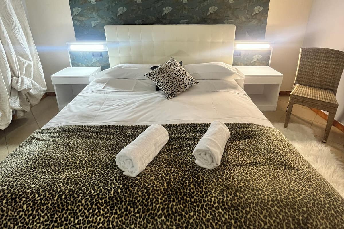 A hotel room with a bed, two bedside tables, a chair, and a wall with a leaf pattern.