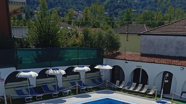 Ein Schwimmbecken mit Sonnenschirmen und Liegestühlen, umgeben von einer gefliesten Terrasse und Blick auf eine gebirgige Landschaft.