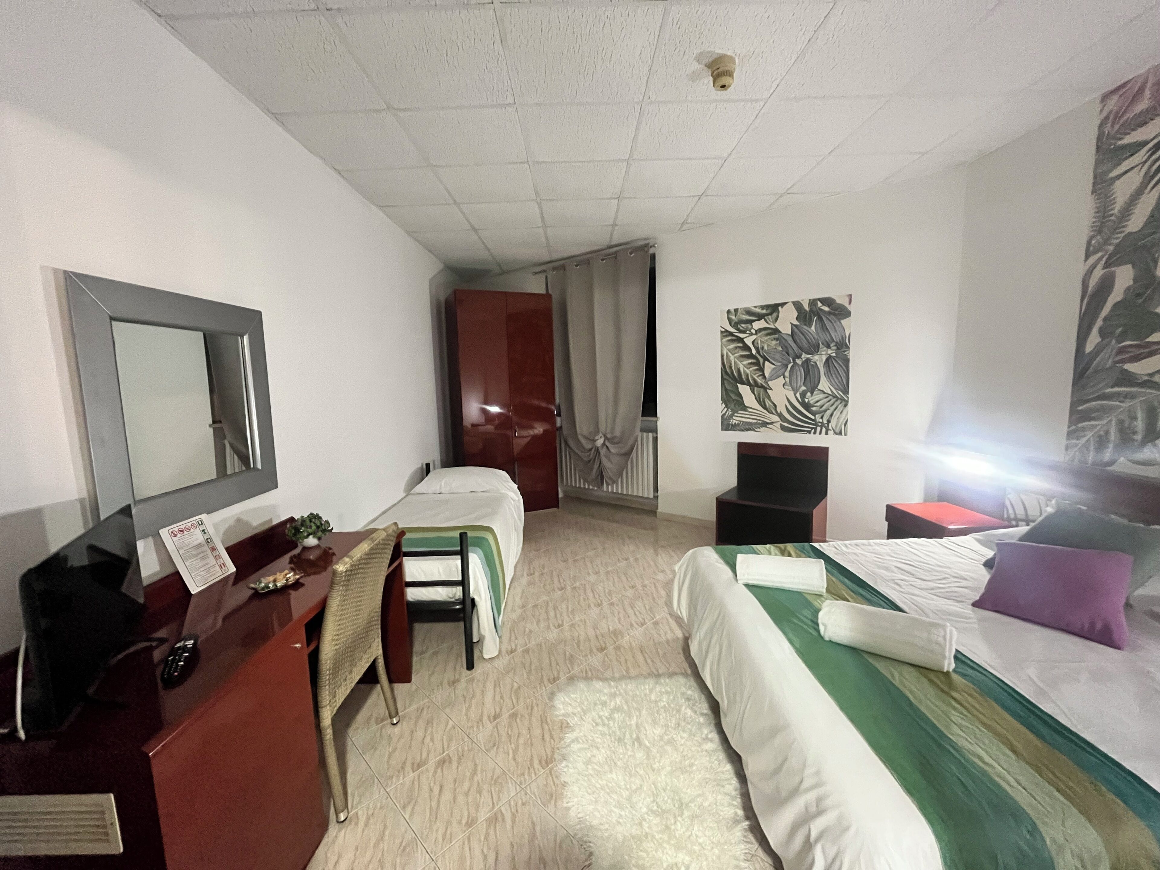 Ein Hotelzimmer mit Bett, Schreibtisch mit Stuhl, Kleiderschrank und einem großen Spiegel.