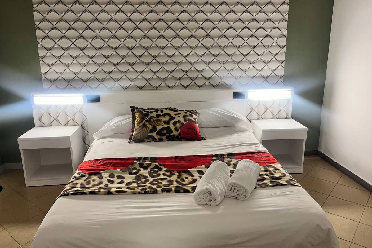 A neatly made bed with a leopard print blanket, a red rose pillow, and two rolled towels.