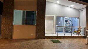 A modern building with a glass door entrance, a small outdoor seating area with a chair, and a visible door leading inside.