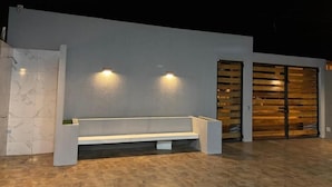A modern building exterior with a bench, two wall-mounted lights, and a wooden door.