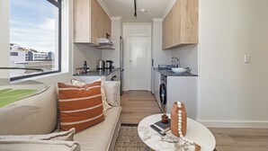 A modern apartment with a living room, kitchen, and dining area. It features a large window, a sofa with decorative pillows, a coffee table, and a view of the city. - The York  | Designer CBD Gem | Spacious Balcony (Cape Town)