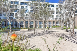 Een modern gebouw met meerdere verdiepingen, balkons en een binnentuin met bomen en grindpaden.