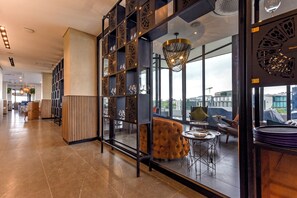 A modern hotel lobby with a glass partition, seating area, and a view of the cityscape. - Live Rosebank. Feel the Vibe. (Johannesburg)