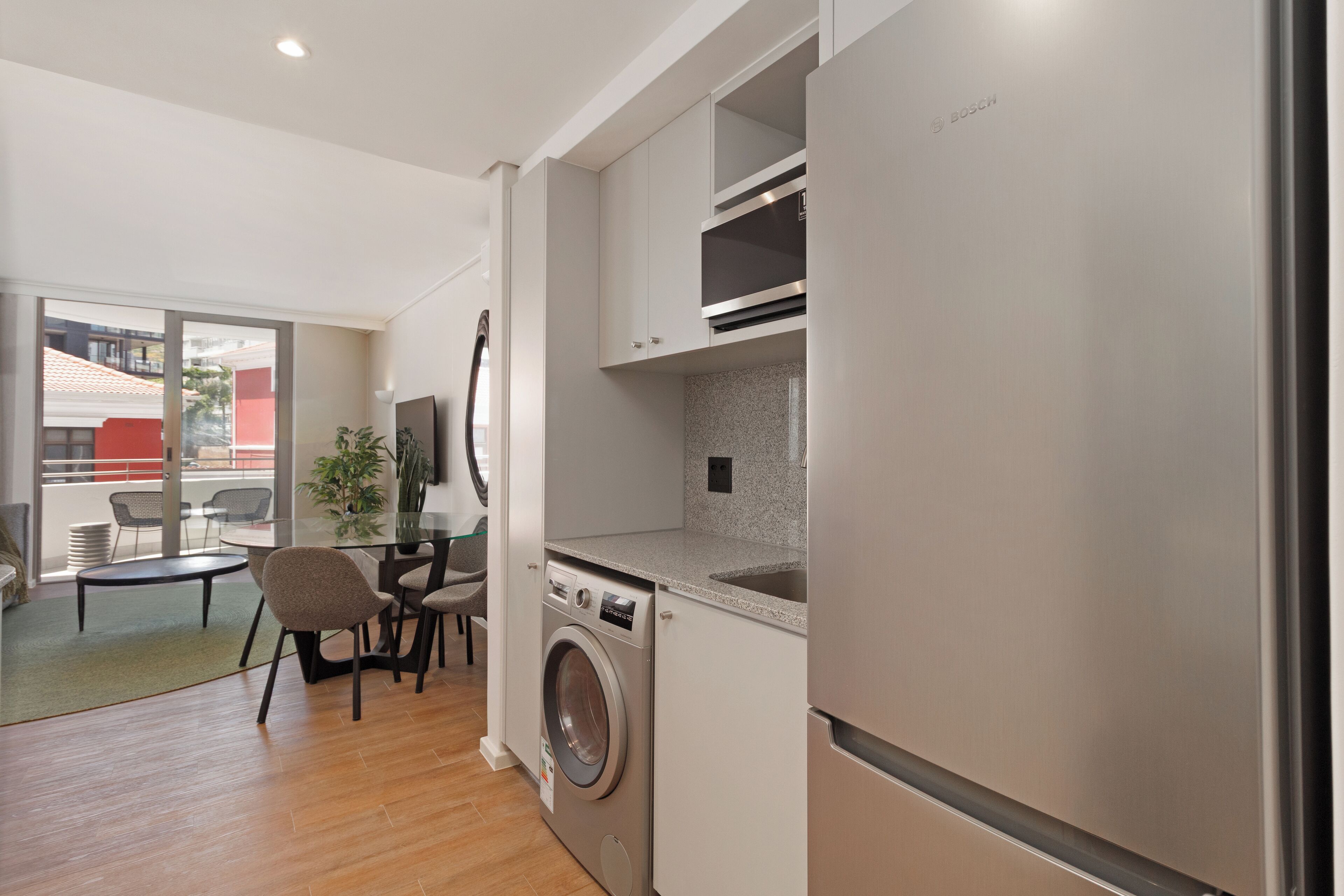 A compact kitchen with a washing machine, a refrigerator, and a dining area with chairs and a table.