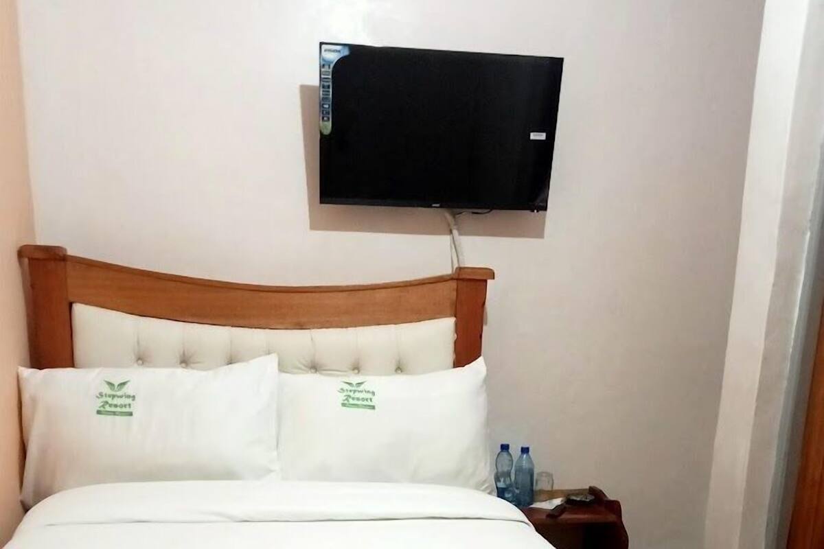 A hotel room with a bed, a television mounted on the wall, and a nightstand with water bottles.