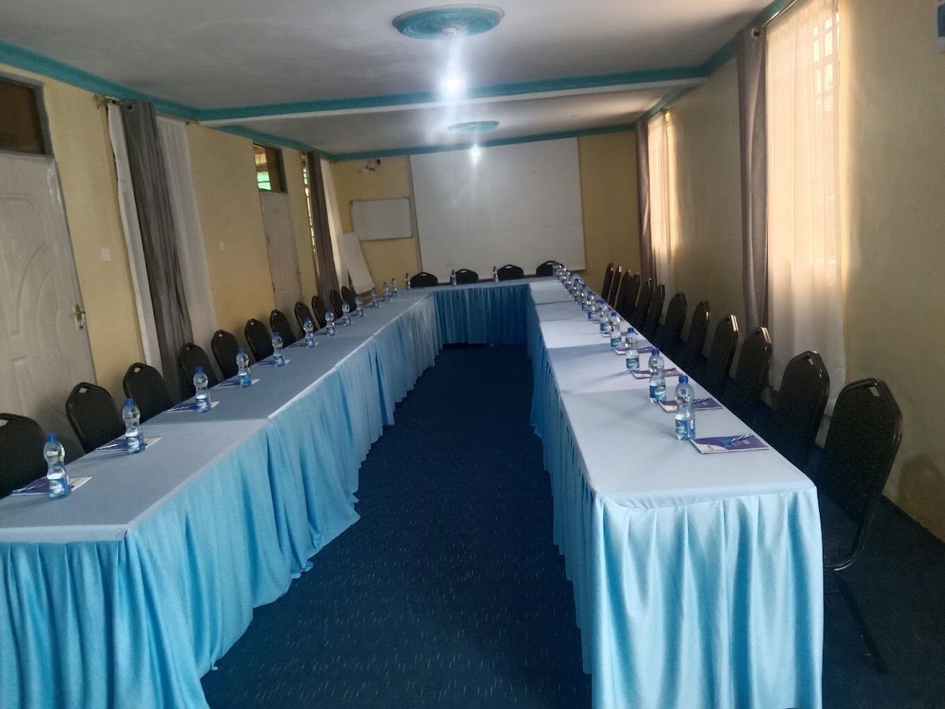 Una sala de conferències amb una taula llarga, cadires, ampolles d'aigua i una pantalla projectora.