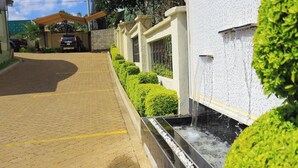A paved driveway leading to a building with a water feature and a covered parking area. - Stepwing Resort (Nyeri)