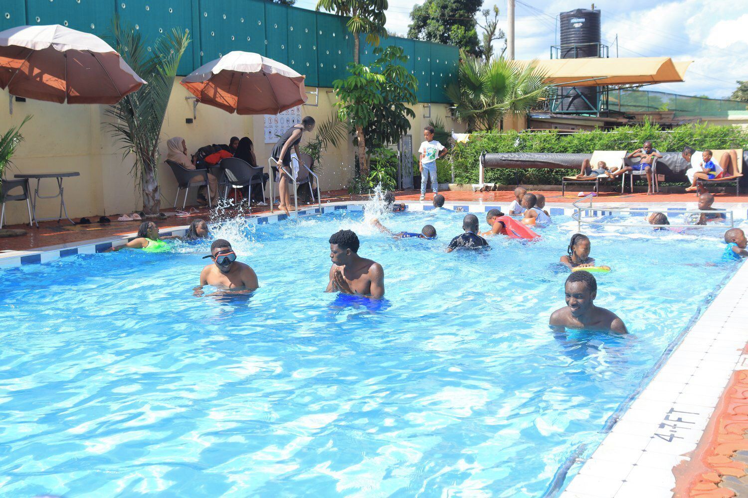 Una piscina con gente en el agua, rodeada de sombrillas y sillas.