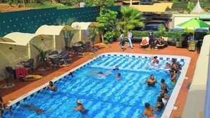 A swimming pool with people swimming and relaxing. There are lounge chairs and umbrellas around the pool. - Stepwing Resort (Nyeri)