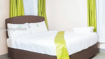 Ein ordentlich gemachtes Bett mit weißen Leinen und einem grünen Akzent, in einem Zimmer mit grünen Vorhängen und einem braunen Kopfteil.