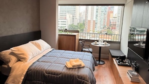 A modern bedroom with a large bed, a small table, and a TV. - New and Comfortable Flat • Olympic Village (São Paulo)