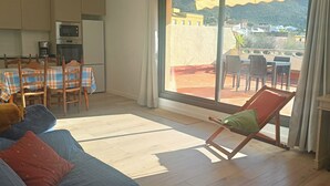Een woonkamer met een bank, een eettafel met stoelen, een keukenhoek en een balkon met uitzicht.