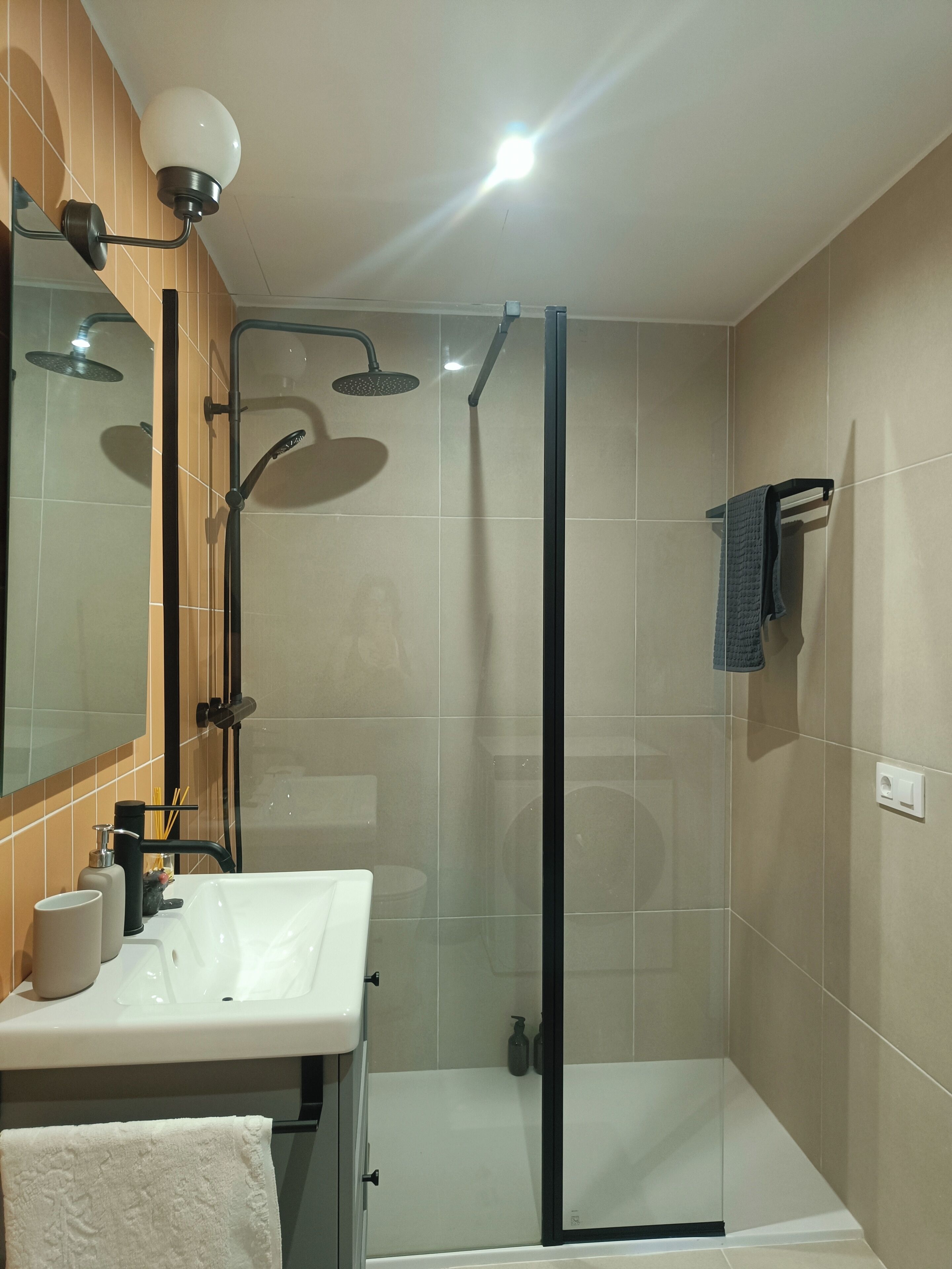 A modern bathroom with a glass-enclosed shower, a white sink, and a mirror above it.